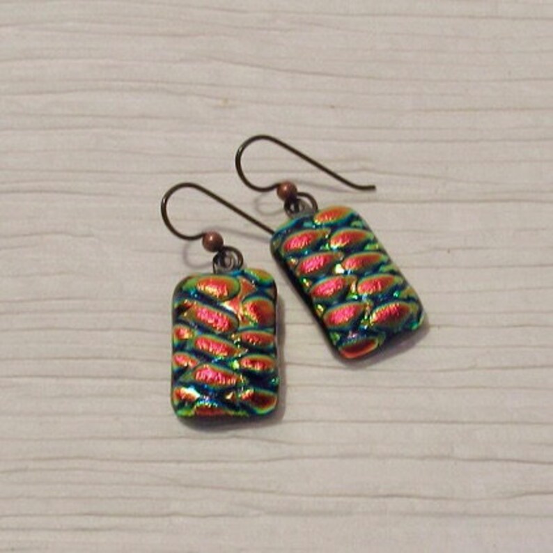 May include: A pair of iridescent glass earrings with a scaly pattern in shades of green, blue, and red. The earrings are attached to silver hooks.