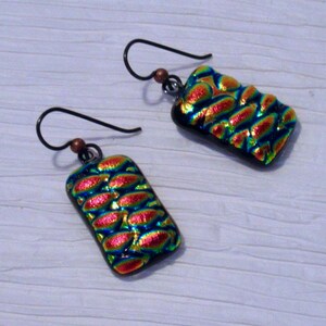 May include: A pair of earrings with iridescent glass rectangular pendants. The glass has a textured pattern and is a mix of red, green, and blue colors.