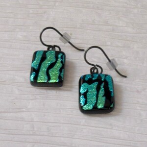 May include: A pair of earrings with black metal hooks and rectangular green and blue glass pendants. The glass has a textured, iridescent finish.