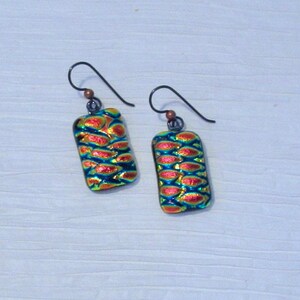 May include: A pair of iridescent glass earrings with a textured, scaly pattern in shades of red, blue, and green. The earrings are rectangular in shape and have silver hooks.