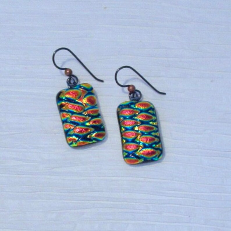 May include: A pair of iridescent glass earrings with a textured, scaly pattern in shades of red, blue, and green. The earrings are rectangular in shape and have silver hooks.