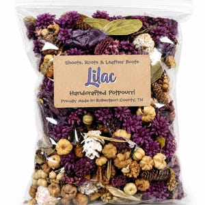 May include: A clear plastic bag filled with handcrafted lilac potpourri. The potpourri includes dried purple flowers, small pine cones, and other natural elements. The bag has a brown label with the word "Lilac" and the text "Shoots, Roots & Leather Boots".