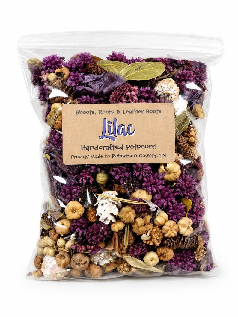 May include: A clear plastic bag filled with handcrafted lilac potpourri. The potpourri includes dried purple flowers, small pine cones, and other natural elements. The bag has a brown label with the word "Lilac" and the text "Shoots, Roots & Leather Boots".