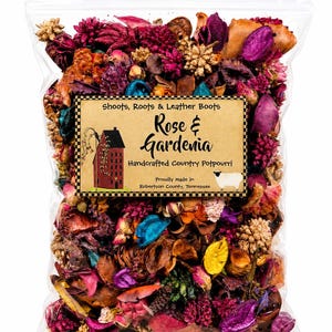 May include: A clear plastic bag filled with colorful dried potpourri including pink, purple, blue, and yellow botanical elements. A rectangular label features the text Shoots, Roots & Leather Boots, Rose & Gardenia, Handcrafted Country Potpourri, and Proudly Made in Robertson County, Tennessee, with an illustration of a red house and a sheep.