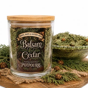 May include: A clear glass jar filled with green dried cedar and balsam potpourri, topped with a light wood lid. The label features the text Shoots, Roots & Leather Boots, Balsam & Cedar, and Handcrafted Potpourri in a decorative font style.