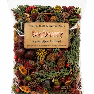 May include: A clear plastic bag filled with potpourri containing green cedar sprigs, brown pinecones, red berries, and dried fruit. A tan label reads: Shoots, Roots & Leather Boots, Bayberry, Handcrafted Potpourri, Proudly Made in Robertson County, Tennessee.