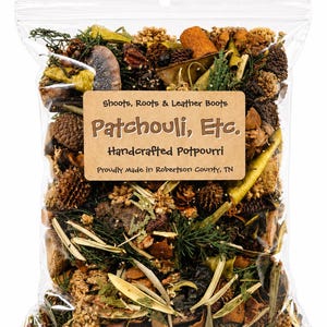 May include: A clear plastic bag filled with handcrafted potpourri. The potpourri includes pine cones, dried leaves, and other natural elements. A brown label reads "Shoots, Roots & Leather Boots Patchouli, Etc. Handcrafted Potpourri Proudly Made in Robertson County, TN."