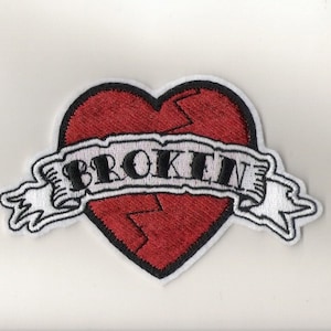 Puede incluir: Un corazón rojo con una grieta en el medio y una pancarta blanca con la palabra "BROKEN" en letras negras.