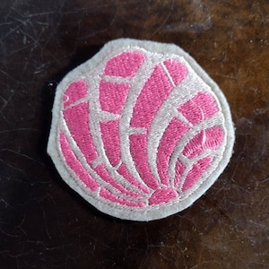 Könnte beinhalten: Ein gestickter Aufnäher in Form einer Concha, einem traditionellen mexikanischen Süßbrot, in Rosa und Weiß.
