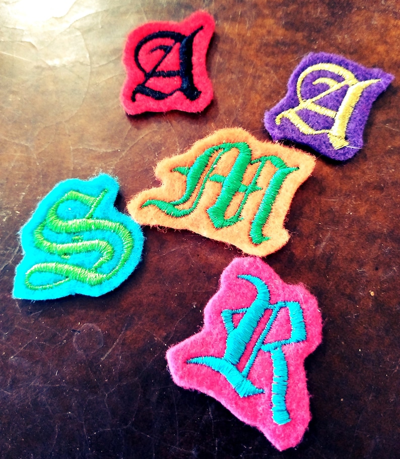 May include: Five felt patches in different colors, each with a letter of the word "SMART" embroidered in a contrasting color. The letters are in a stylized, old-fashioned font.