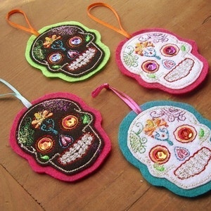 May include: Four felt sugar skull ornaments with colorful embroidery and sequins. The ornaments are in green, pink, white, and blue.