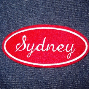 May include: Red oval-shaped patch with white embroidered lettering that reads "Sydney".