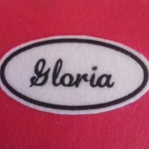 May include: White oval-shaped patch with a black border and the name "Gloria" embroidered in black cursive lettering.