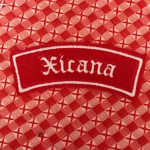 Könnte beinhalten: Roter Stoff-Patch mit weiß gesticktem Schriftzug "Xicana".