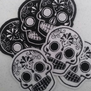 May include: Five black and white embroidered sugar skull patches. The skulls are decorated with intricate floral designs.