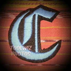 Op de afbeelding: Een blauwe en zwarte geborduurde strijk-op patch in de vorm van de letter C. De letter is in een gotische lettertype.