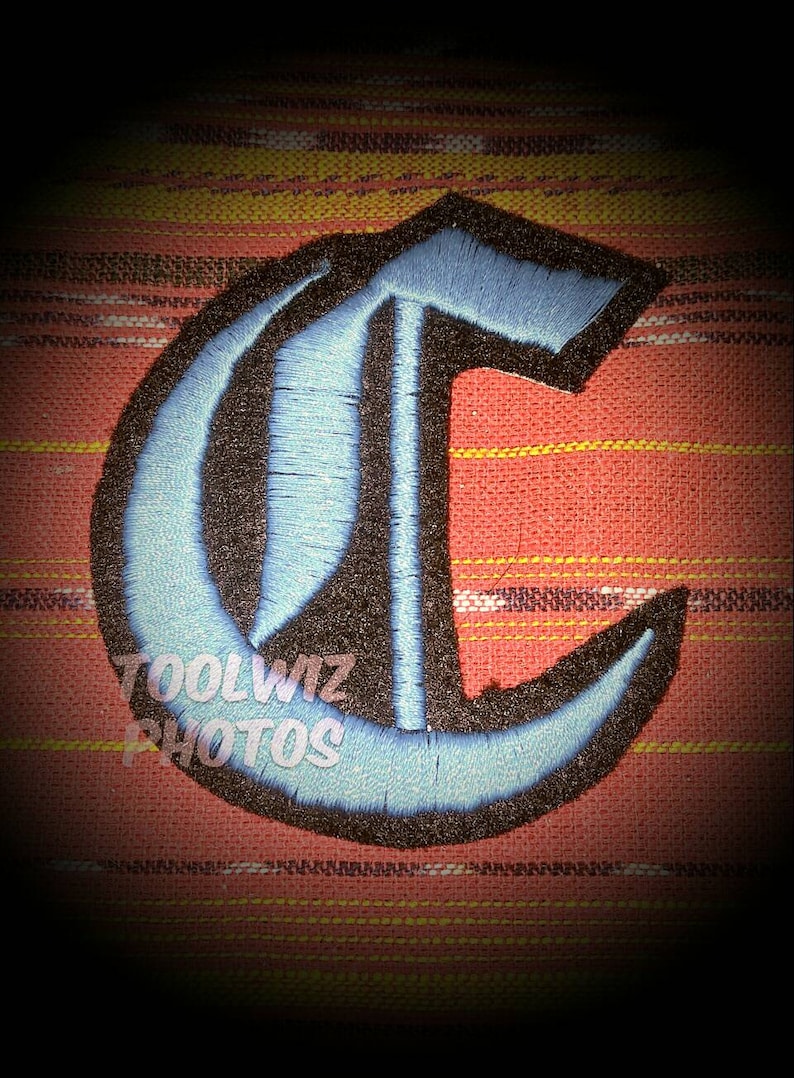 Op de afbeelding: Een blauwe en zwarte geborduurde strijk-op patch in de vorm van de letter C. De letter is in een gotische lettertype.
