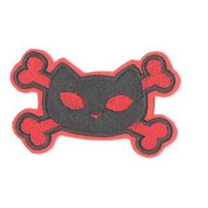 May include: Embroidered patch featuring a black cat skull design with red eyes and crossbones. The patch has a red border and is suitable for application on clothing or accessories. The cat skull design is a unique and edgy style.