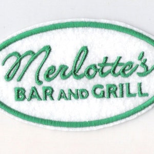 Puede incluir: Parche ovalado bordado en verde sobre fondo blanco. El texto dice "Merlotte's Bar and Grill".