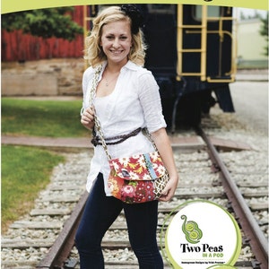 May include: A woman wearing a white shirt, blue jeans, and a colorful floral crossbody bag. The bag has a brown strap and is worn over her shoulder. The image is set against a backdrop of railroad tracks and a train.
