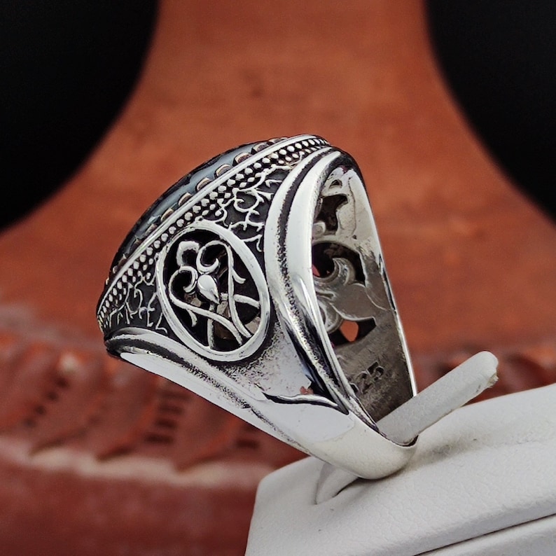 May include: A silver ring with an intricate design and a dark blue stone. The ring has a detailed pattern on the band and a large oval-shaped stone in the center.
