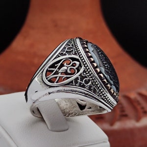 May include: A silver ring with an ornate design and a black onyx stone. The ring has a detailed filigree pattern and a bezel setting for the stone.