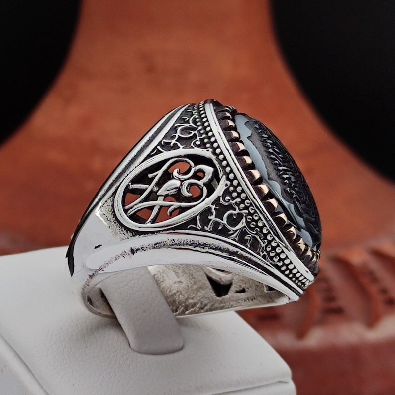 May include: A silver ring with an ornate design and a black onyx stone. The ring has a detailed filigree pattern and a bezel setting for the stone.