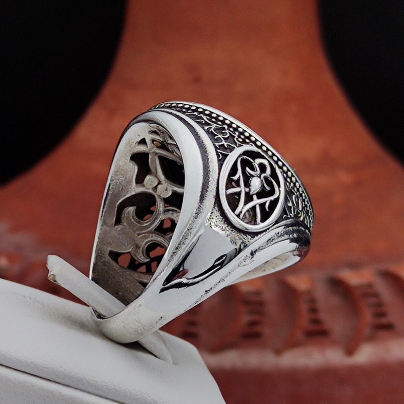 May include: A silver ring with an intricate design featuring a circular cutout with a floral motif. The ring is made of sterling silver and has a polished finish.