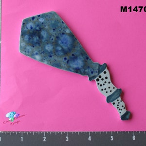 May include: A blue and white ceramic spatula with a speckled glaze and a black and white polka dot handle. The spatula is shaped like a fish with a long, thin tail.