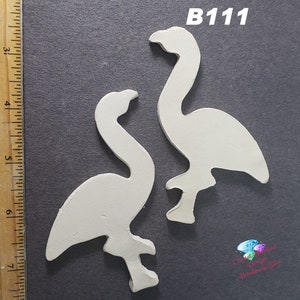 May include: Two white unfinished wooden flamingo shapes. The shapes are approximately 5 inches tall. The shapes are on a gray background. The text "B111" is in the upper right corner of the image.