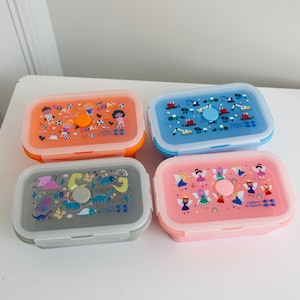 Puede incluir: Cuatro loncheras coloridas con diferentes diseños. Las loncheras están hechas de silicona y tienen una tapa con cierre. Los diseños incluyen dinosaurios, hadas, vehículos de construcción y jugadores de fútbol.