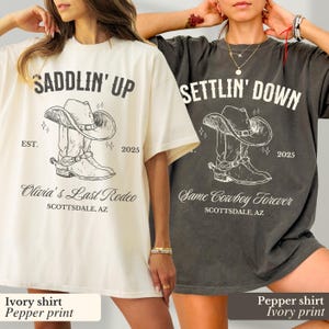 May include: Two oversized t-shirts with a cowboy boot and hat graphic. The ivory shirt has the text "SADDLIN' UP EST. 2025 Olivia's Last Rodeo SCOTTSDALE, AZ". The pepper shirt has the text "SETTLIN' DOWN 2025 Same Cowboy Forever SCOTTSDALE, AZ".