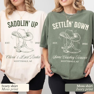 May include: Two t-shirts with a cowboy boot and hat graphic. The ivory shirt has the text "Saddlin' Up" and "Olivia's Last Rodeo" with the location "Scottsdale, AZ". The moss green shirt has the text "Settlin' Down" and "Same Cowboy Forever" with the location "Scottsdale, AZ".