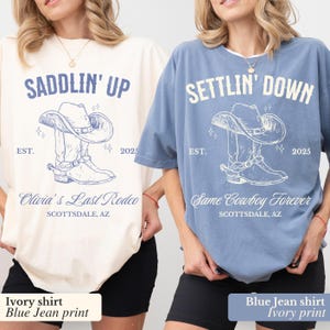 May include: Two t-shirts with a cowboy boot and hat design. The ivory shirt says "Saddlin' Up" and "Olivia's Last Rodeo" with the date "EST. 2025". The blue shirt says "Settlin' Down" and "Same Cowboy Forever" with the date "EST. 2025".