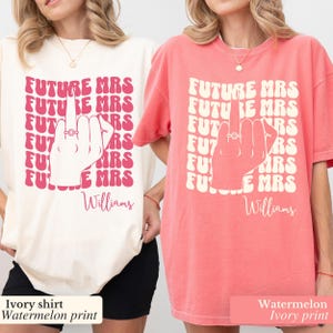 May include: Two t-shirts with a pink graphic of a hand with a ring on the middle finger. The text on the shirts reads "FUTURE MRS" repeated multiple times and "Williams" at the bottom. One shirt is ivory with a watermelon print and the other is watermelon with an ivory print.