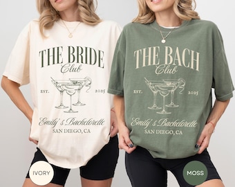 May include: Two t-shirts, one ivory and one moss green, with a graphic of three martini glasses and the text "The Bride Club" and "The Bach Club" with the text "Emily's Bachelorette San Diego, CA" below.