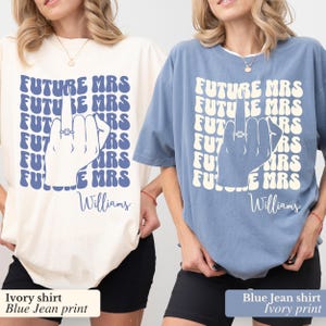 May include: Two t-shirts, one ivory and one blue jean, with a graphic print of a hand with a ring on the finger and the text "FUTURE MRS" repeated in a retro font. The text "Williams" is printed below the graphic on both shirts.