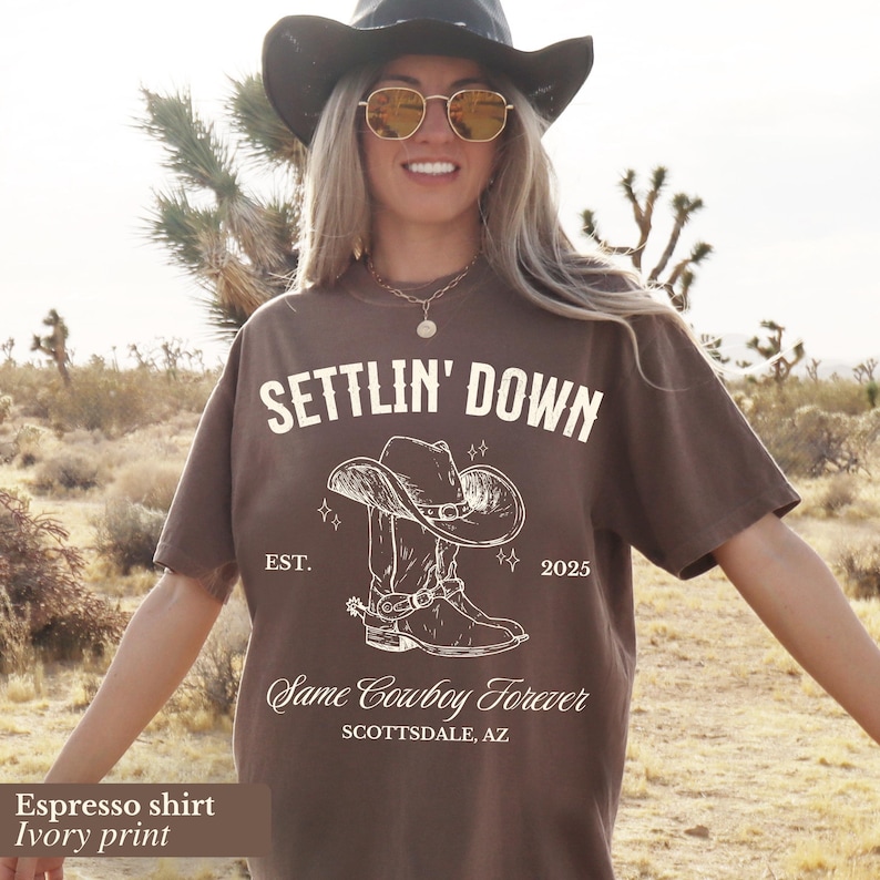 May include: Espresso brown t-shirt with an ivory print of a cowboy boot and hat with the text "Settlin' Down"  "Est. 2025" and "Same Cowboy Forever"  "Scottsdale, AZ"