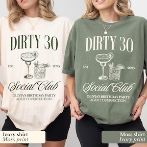 Könnte beinhalten: Zwei T-Shirts mit einem grafischen Design eines Cocktailglases und eines Schnapsglases mit dem Text "Dirty 30 Social Club Olivia's Birthday Party Aged to Perfection" bedruckt. Das Shirt auf der linken Seite ist elfenbeinfarben mit einem moosgrünen Druck. Das Shirt auf der rechten Seite ist moosgrün mit einem elfenbeinfarbenen Druck.