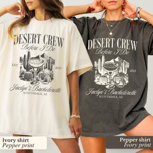 May include: Two oversized t-shirts, one ivory and one pepper, featuring a desert-themed graphic. The design includes text that reads "DESERT CREW Before I Do" with a margarita, cactus, and ring illustration. The text "Jaclyn's Bachelorette Scottsdale, AZ" is also present.