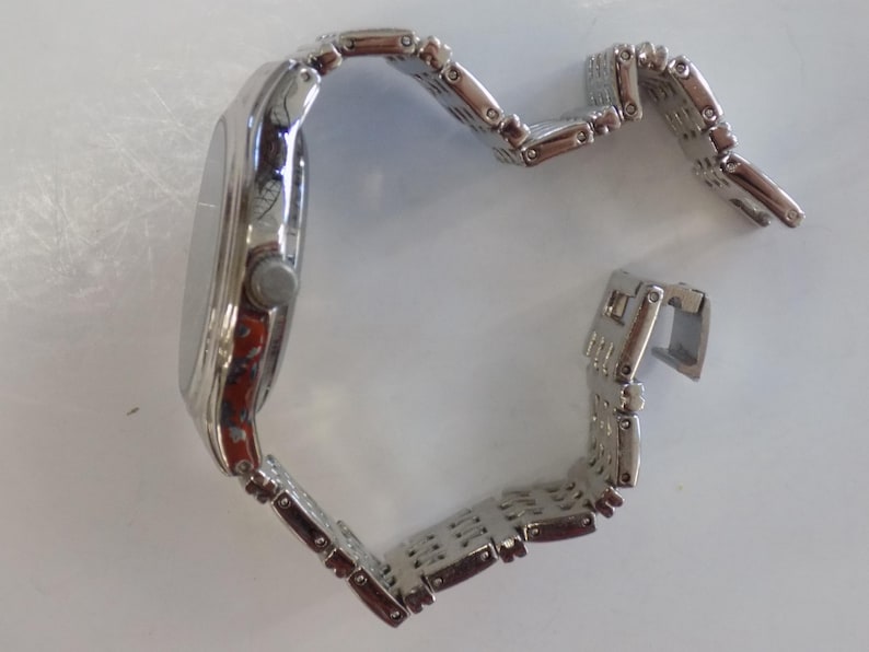 Puede incluir: Un reloj plateado con una correa de metal plateado. El reloj tiene una esfera redonda y una correa de metal plateado.