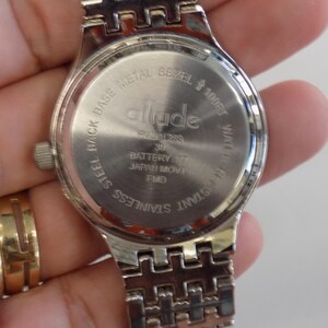 Puede incluir: Un reloj de pulsera de acero inoxidable plateado con un bisel de metal plateado y una correa plateada. La esfera del reloj est&aacute; marcada con la palabra "allude" y el texto "Steel Back Base Metal Bezel 100ft Water Resistant Stainless Steel".