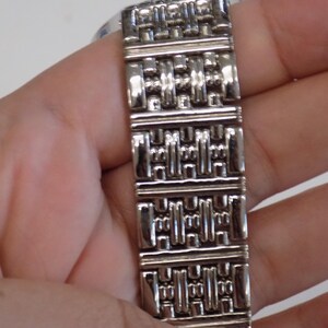 Puede incluir: Pulsera de reloj plateada con un patr&oacute;n geom&eacute;trico.