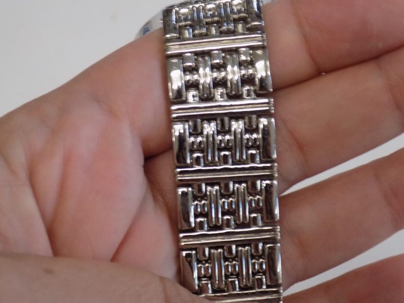 Puede incluir: Pulsera de reloj plateada con un patr&oacute;n geom&eacute;trico.