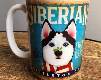 Peut inclure: Mug en céramique blanche avec un Husky sibérien aux yeux bleus, portant une écharpe rayée rouge et blanche et du gui. Le mug affiche les mots "Siberian Mistletoe Co." et "Fresh Daily" sur un fond bleu.