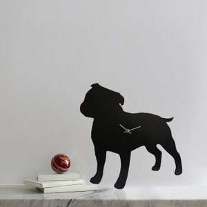 May include: Black silhouette of a dog, possibly a Staffordshire Bull Terrier, used as a wall clock. The clock hands are visible and a red ball is in the foreground.