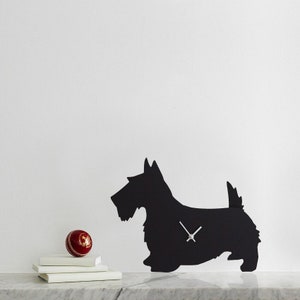 May include: Black silhouette of a Scottish Terrier dog with clock hands in the center. The clock is on a white surface with a red ball and books.