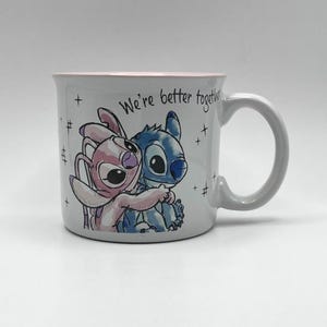 May include: A white ceramic mug featuring a cartoon illustration of Stitch and Angel embracing. The mug has a pink rim and the words "We're better together" are written on the side. The mug has a gray handle.