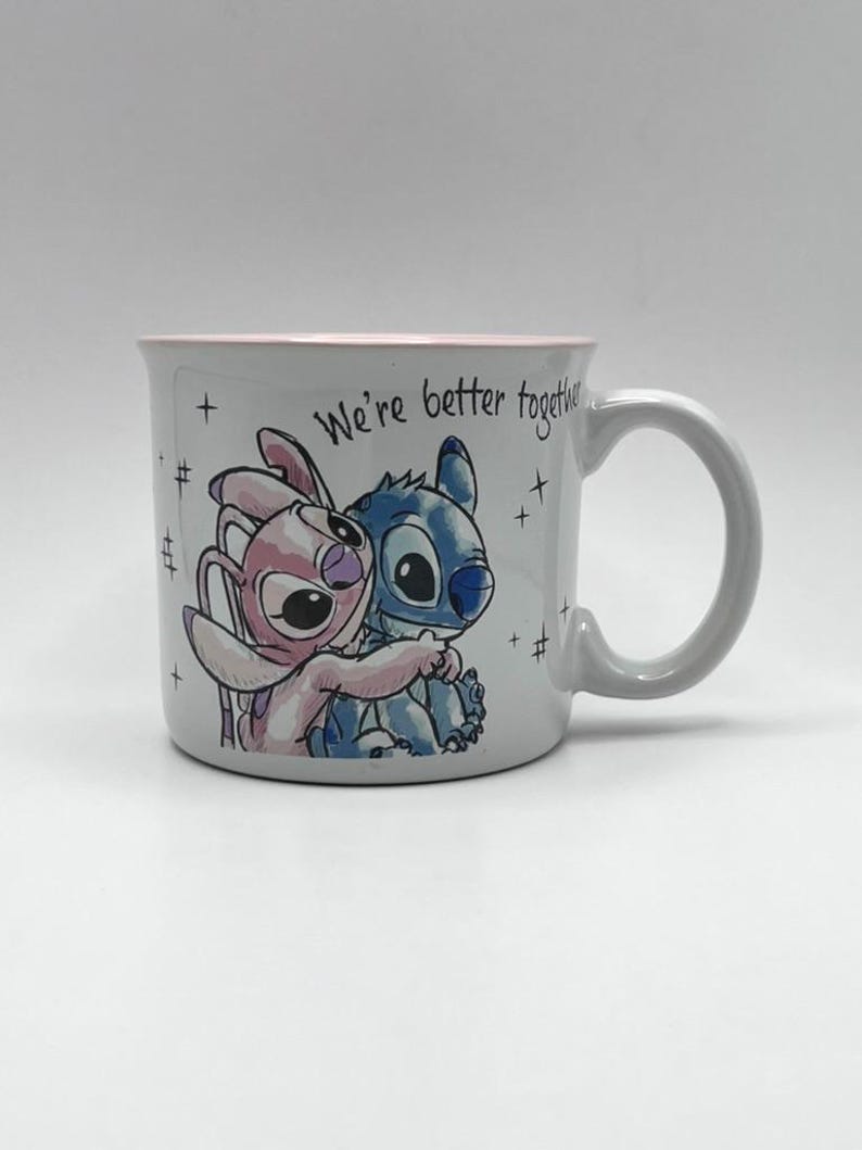 May include: A white ceramic mug featuring a cartoon illustration of Stitch and Angel embracing. The mug has a pink rim and the words "We're better together" are written on the side. The mug has a gray handle.