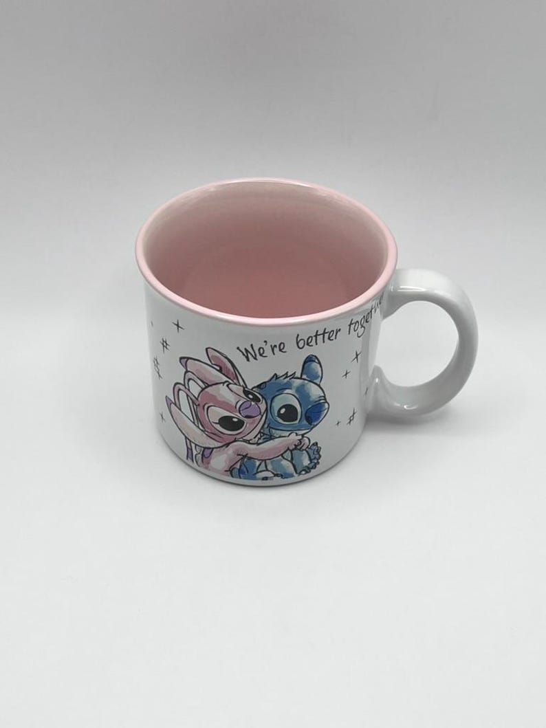 May include: White ceramic mug with a pink interior and handle. The mug features a colorful illustration of two cartoon characters embracing, with the text "We're better together" written on the side. The mug is a standard size.